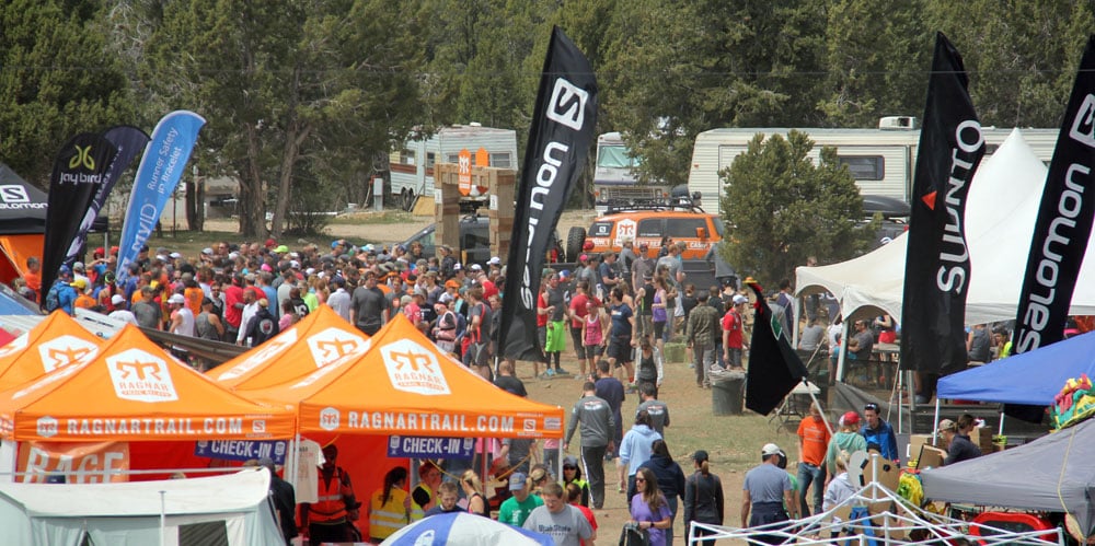 A large crowd gathers around vendor tents and banners at an outdoor event.